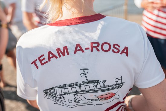 Back view of a white T-shirt with a red collar and a TEAM A-ROSA print along with a illustration of a ship.
