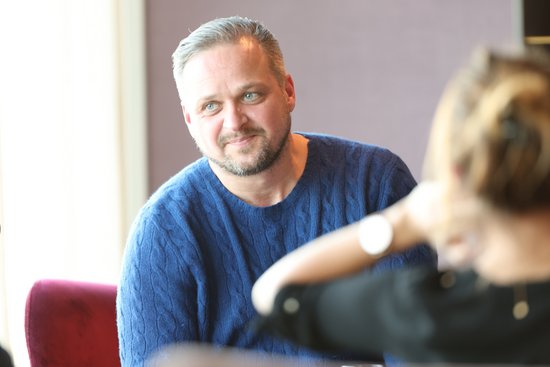 Man in a blue sweater with a short beard smiles at a woman with her hair up.