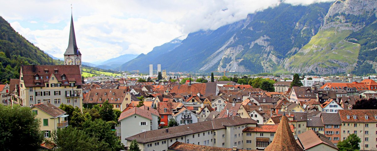 View of the old town of Chur with historic buildings, a church with a tall tower, and mountains in the background