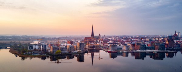 An aerial view of Rostock at sunrise with a view of the city, the harbor, and the reflecting water surfaces.