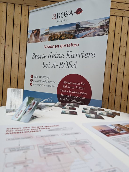 A-ROSA advertising banner with the text Start your career at A-ROSA and contact details for applications, informational materials lying on a table.