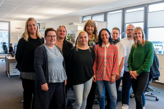 Team ASC from A-ROSA with nine people in a modern office, standing in front of desks and windows.